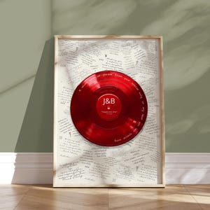 May include: A framed wall art piece featuring a glossy red vinyl record centered on a white background covered in repeated handwritten text. The record label displays the letters J&B in white, with text around the rim reading A short lyrics or phrase from your special song or any text you like special song.