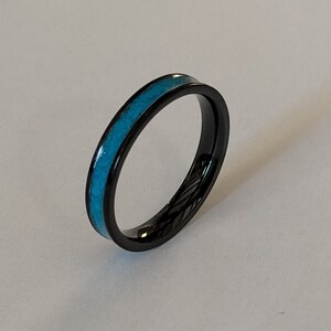 以下が含まれることがあります： 黒い指輪、ターコイズの象嵌入り。指輪は細いバンドと研磨仕上げです。ターコイズの象嵌は、黒い金属に対して明るく対照的な色です。