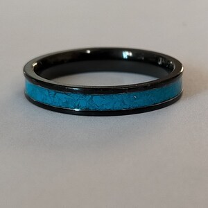 以下が含まれることがあります： 黒いリング、ターコイズのインレイ付き。 リングはミニマリストデザインで、黒い金属バンドと質感のあるターコイズの中央部があります。 スタイリッシュなアクセサリーです。