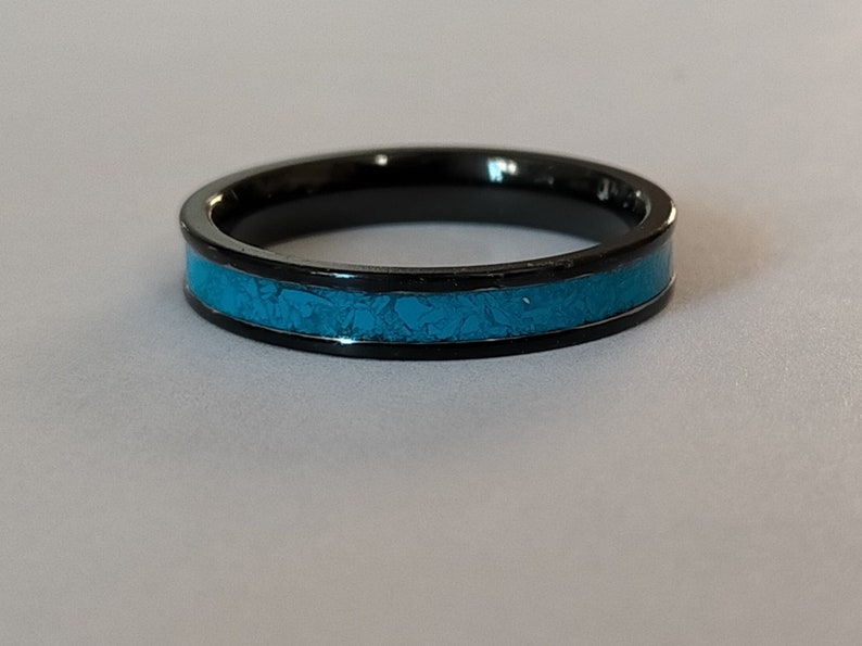 以下が含まれることがあります： 黒いリング、ターコイズのインレイ付き。 リングはミニマリストデザインで、黒い金属バンドと質感のあるターコイズの中央部があります。 スタイリッシュなアクセサリーです。