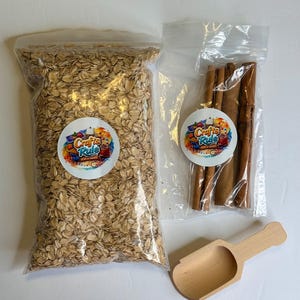 May include: A clear plastic bag filled with rolled oats, a smaller clear plastic bag containing four whole cinnamon sticks, and a small wooden scoop. Both bags feature a circular white sticker with the text Crafts Rule Play & Create.
