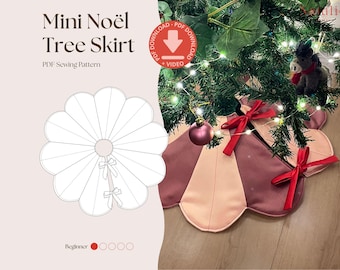 May include: A Mini Noël Tree Skirt PDF sewing pattern featuring a scalloped edge design. The physical skirt is made of alternating dusty rose and light pink fabric panels, accented with two bright red ribbon bows at the center opening.