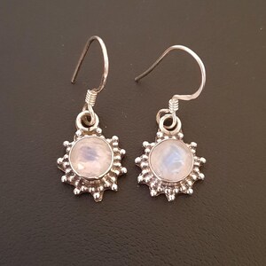 May include: A pair of silver earrings with a round moonstone gemstone set in a sunburst design.
