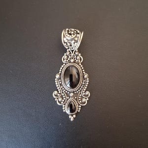 Colgante de plata 925 con dos piedras  negras ovaladas. El colgante está realizado y decorado con filigrana alrededor de las piedras.