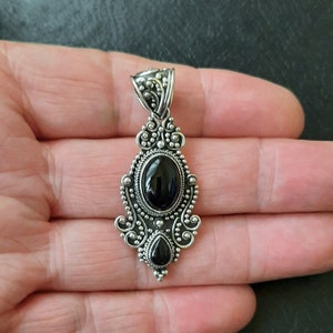 Colgante de plata y onix cabujón con dos piedras de ónix negro. Una mas grande en la parte superior ovalada y otra más pequeña con forma de lágrima en la parte inferior.
Alrededor de las piedras tiene decoración de filigrana.