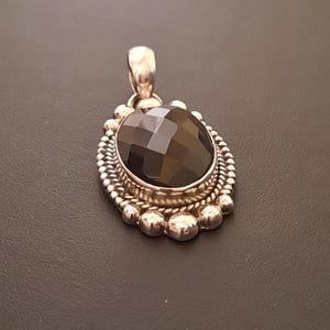 May include: An oval pendant featuring a faceted black gemstone set in a silver frame. The setting is decorated with a twisted rope border and a series of small silver spheres along the outer edge, topped with a silver bail for attachment.