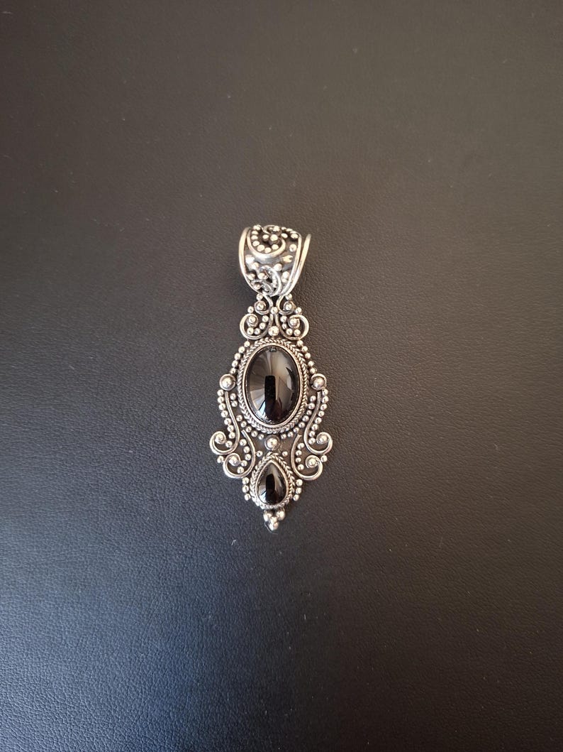 Colgante de plata 925 con dos piedras  negras ovaladas. El colgante está realizado y decorado con filigrana alrededor de las piedras.