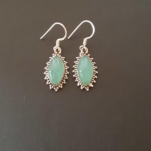 May include: A pair of silver earrings with green gemstone accents. The earrings have a delicate, ornate design.