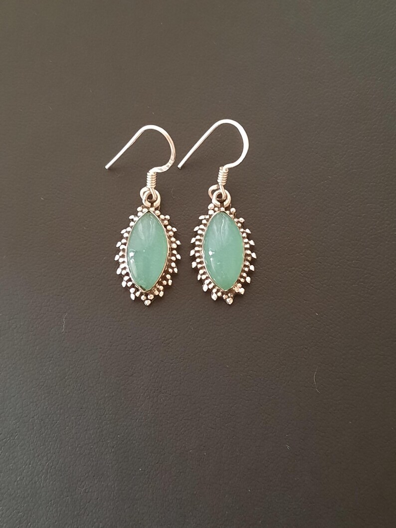 May include: A pair of silver earrings with green gemstone accents. The earrings have a delicate, ornate design.