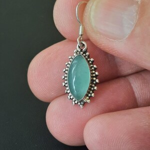 May include: Silver dangle earrings with a light blue oval gemstone set in a silver filigree design.