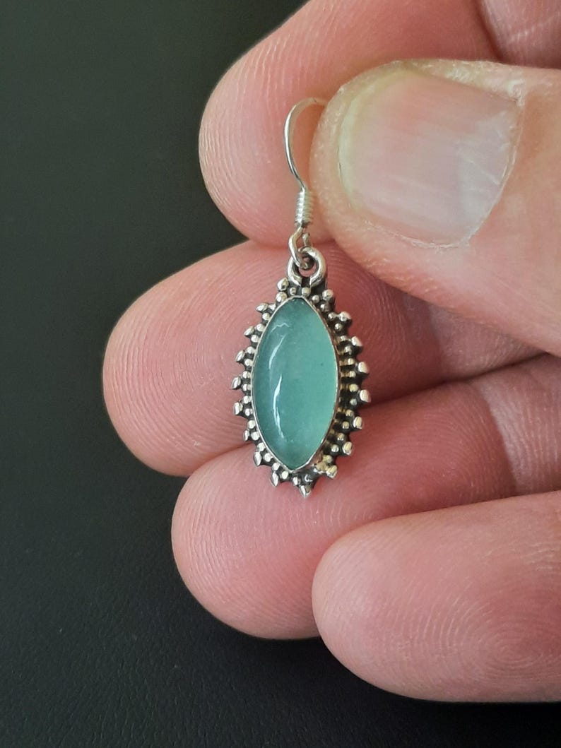 May include: Silver dangle earrings with a light blue oval gemstone set in a silver filigree design.