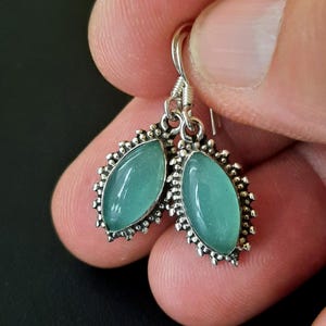 May include: A pair of silver earrings with a teal green stone set in a decorative silver frame.