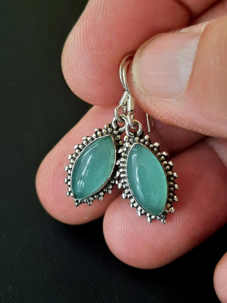 May include: A pair of silver earrings with a teal green stone set in a decorative silver frame.