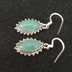 May include: A pair of silver earrings with green gemstone accents. The earrings have a delicate, ornate design.