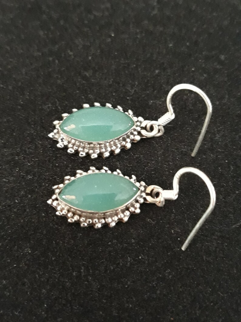 May include: A pair of silver earrings with green gemstone accents. The earrings have a delicate, ornate design.
