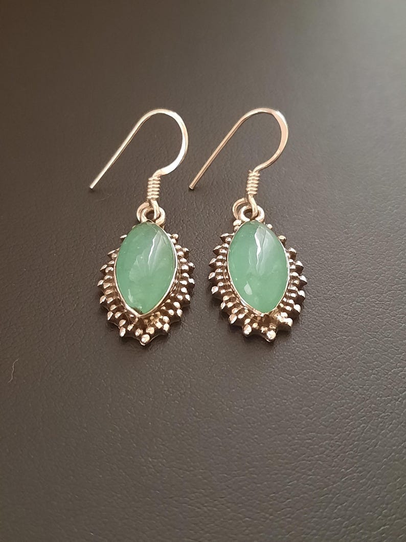 May include: A pair of silver earrings with green oval-shaped stones set in a decorative silver frame. The earrings have a hook closure.
