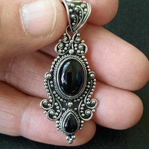 Piedra central ovalada rodeada de filigrana y bolitas de plata de varios tamaños, en la parte inferior piedra en forma de lagrima mas pequeña, con tres bolitas que decoran la farte inferior.