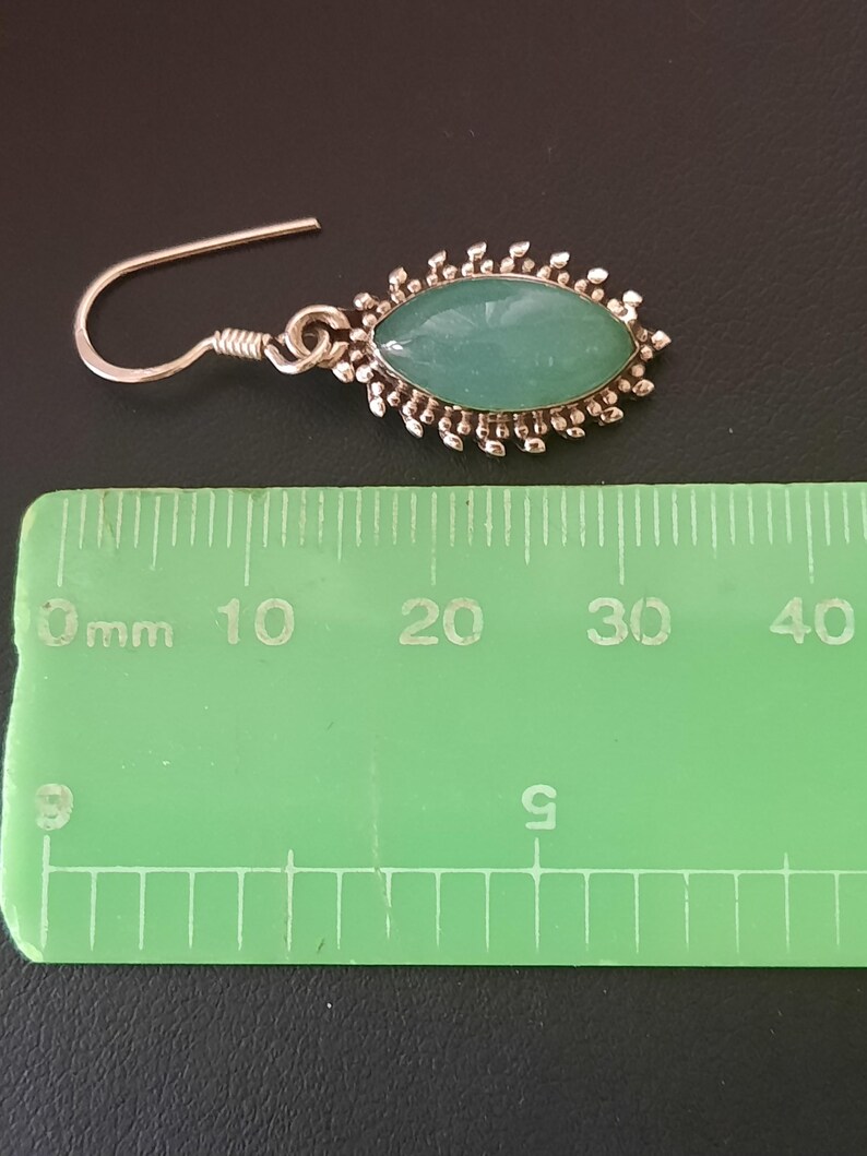 May include: Silver dangle earrings with a green oval gemstone set in a silver filigree design. The earrings measure approximately 2 cm in length.
