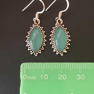May include: A pair of silver earrings with a light blue oval-shaped gemstone set in a silver filigree design. The earrings are approximately 2 cm long.