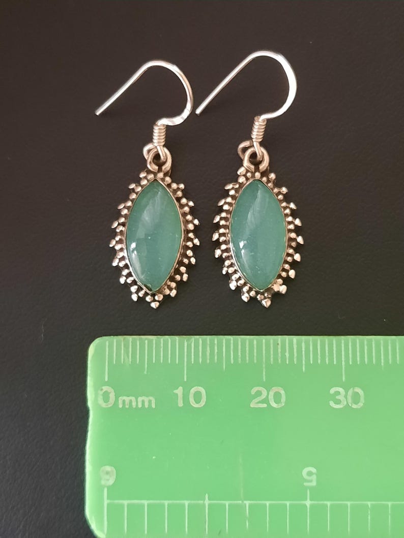 May include: A pair of silver earrings with a light blue oval-shaped gemstone set in a silver filigree design. The earrings are approximately 2 cm long.