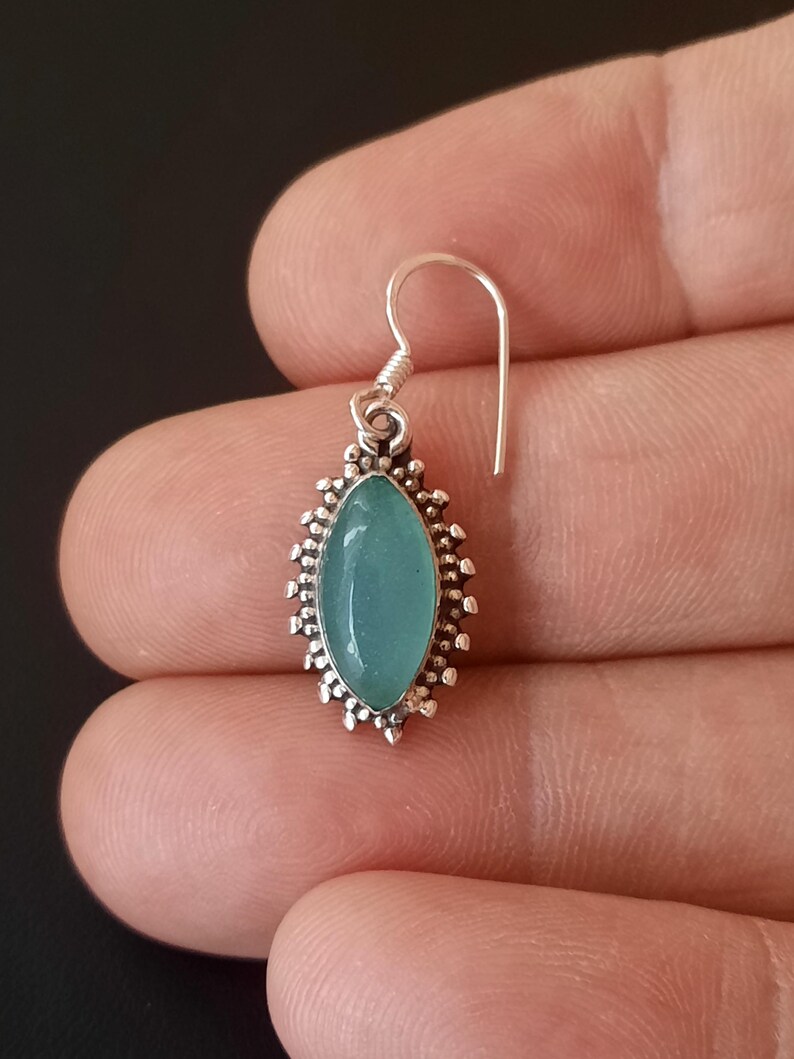 May include: A silver earring with a light blue gemstone set in a decorative silver frame. The earring has a simple hook closure.