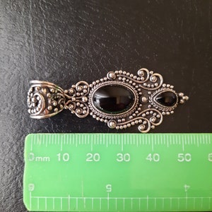 Puede incluir: Un colgante de plata con dos piedras preciosas negras engastadas en un dise&ntilde;o filigranado detallado. El colgante mide aproximadamente 5 cm de largo.
