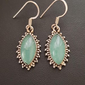 May include: A pair of silver earrings with a light blue oval-shaped gemstone set in a silver filigree design.