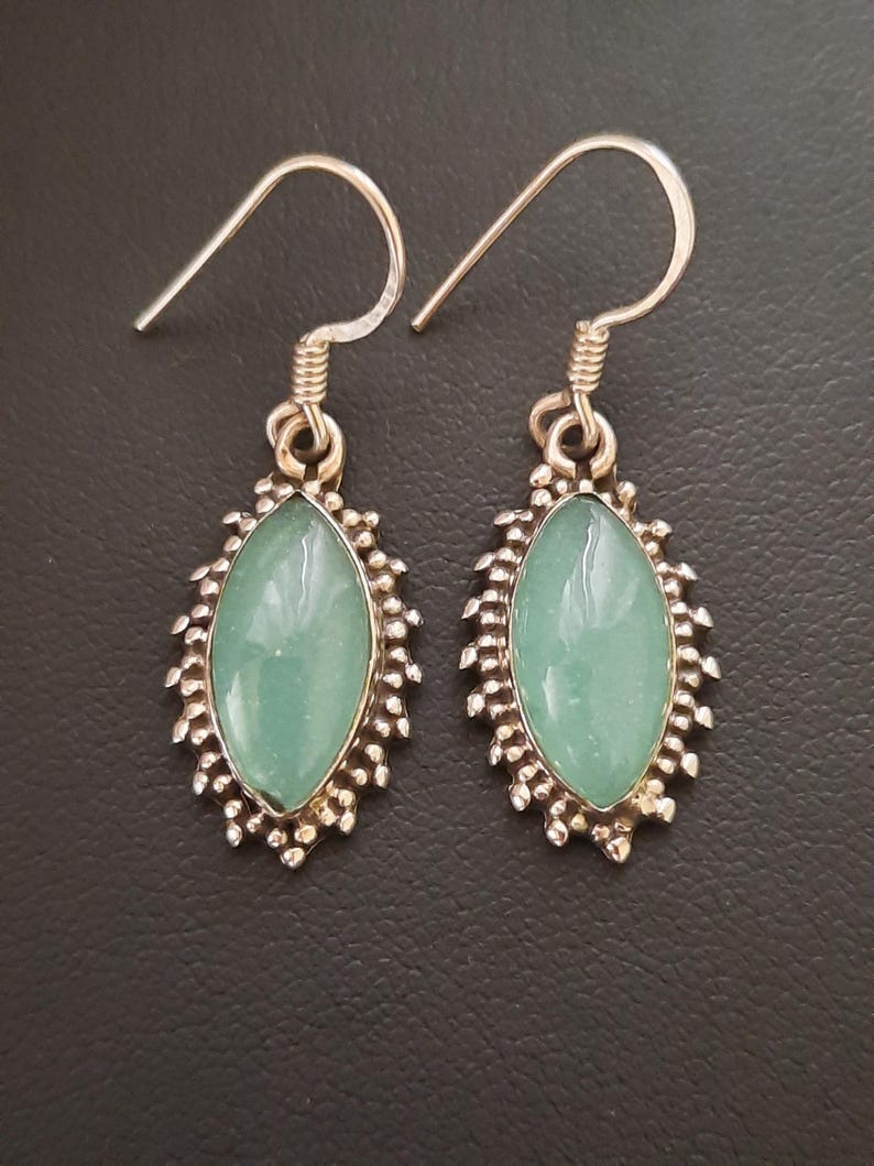 May include: A pair of silver earrings with a light blue oval-shaped gemstone set in a silver filigree design.