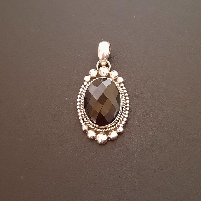 Colgante ovalado de plata con piedra de ónix negro facetada. 
El colgante está decorado alrededor de la piedra con bolitas e hilo torzal de plata.