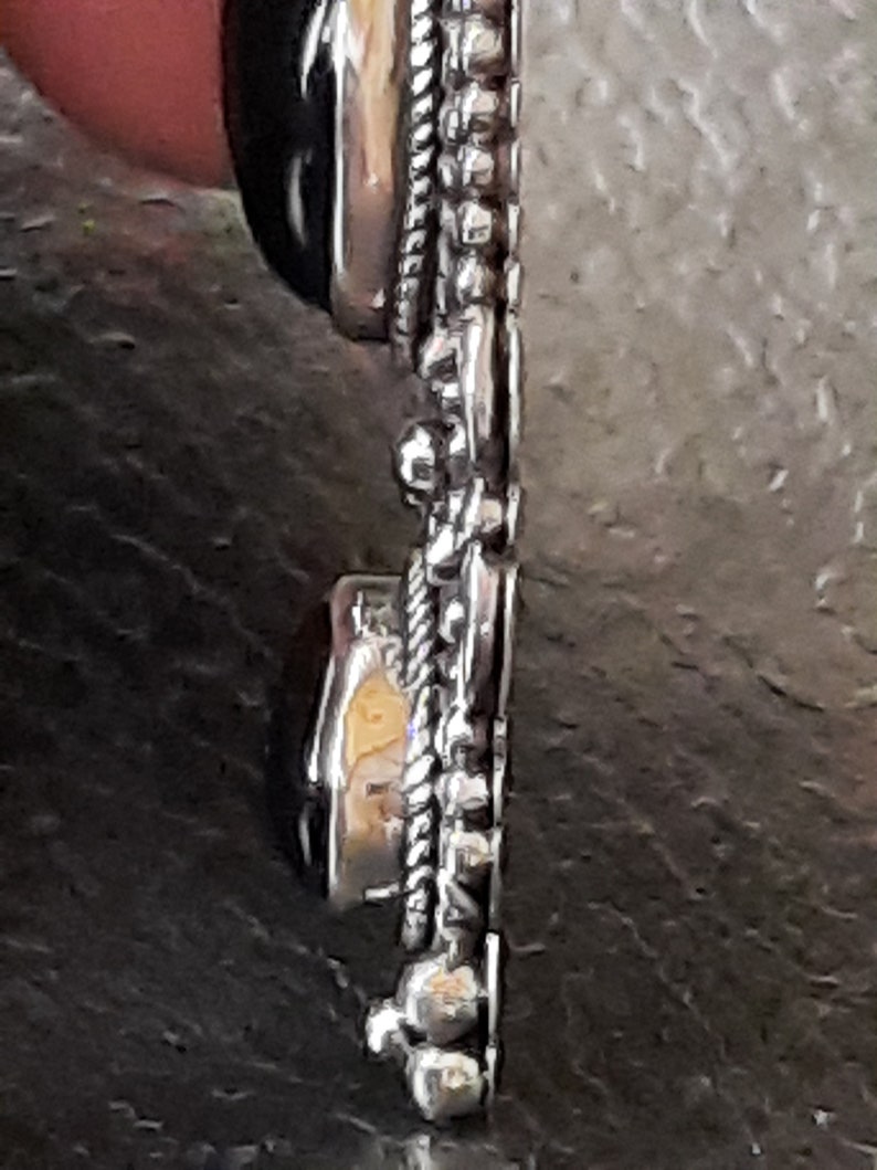 Puede incluir: Un colgante de plata con una piedra preciosa negra y una piedra preciosa transparente. El colgante tiene un dise&ntilde;o detallado con un borde de cuerda y peque&ntilde;as cuentas.
