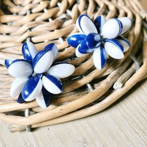 Könnte beinhalten: Ein Paar blaue und weiße Ohrringe in Blumenform. Jeder Ohrring besteht aus mehreren kleinen, runden Perlen, die in Blumenform angeordnet sind. Die Perlen wechseln sich in Blau und Weiß ab.
