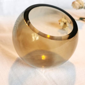 May include: A clear glass bowl with a brown tint and a rounded shape. The bowl is sitting on a white surface.