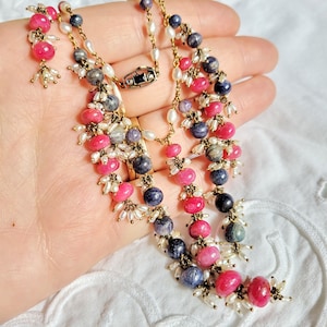 Op de afbeelding: Een meerstrengige ketting met roze, blauwe en witte kralen. De ketting is gemaakt van parels, edelstenen en metaal.