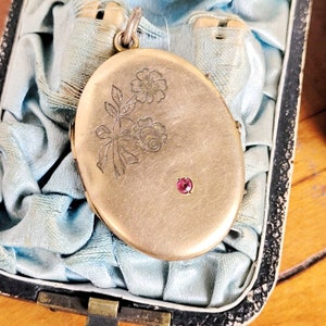 Peut inclure: Médaillon ovale en or avec un motif floral gravé et une seule pierre précieuse rouge.