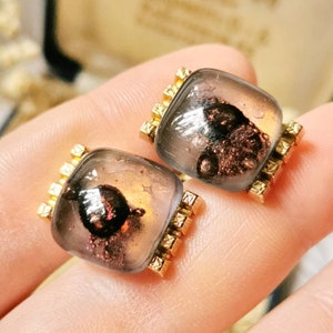 May include: A pair of gold cufflinks with clear glass insets. The glass insets have a brown and silver flecked design.