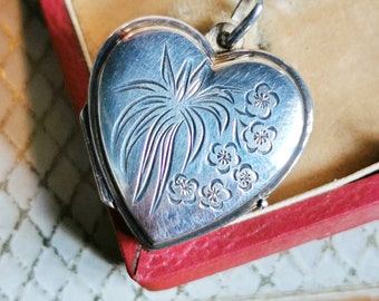 May include: A silver heart-shaped locket with an engraved design of a tree and flowers. The locket is in a red box.