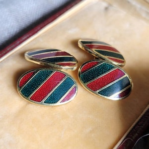 Peut inclure: Quatre boutons de manchette dans un coffret doublé de velours. Les boutons de manchette sont de forme ovale avec un bord doré et un motif rayé rouge, vert et noir.