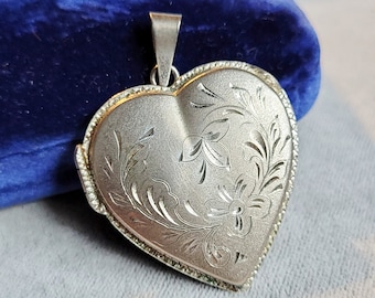 May include: A silver heart-shaped locket with an engraved floral design. The locket has a hinged opening and a loop for attaching a chain.