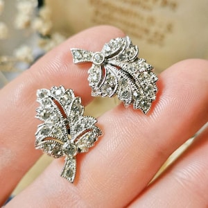 May include: A pair of silver tone earrings with a leaf design and clear rhinestones.