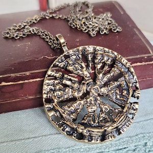 Peut inclure: Un collier avec un pendentif rond en or, au design complexe. Le pendentif présente un motif texturé détaillé avec un élément central en relief. Le collier est sur une chaîne avec un fermoir à mousqueton.