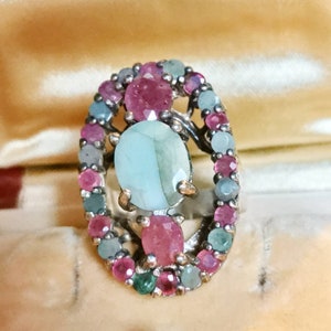 May include: A silver ring featuring a large oval green gemstone surrounded by smaller pink and green gemstones.