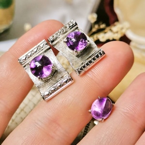 May include: Three silver rings with purple amethyst gemstones. The rings are set in a rectangular shape with a decorative border.
