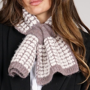 May include: A brown and white knitted scarf with a heart pattern. The scarf is worn by a person with long brown hair.