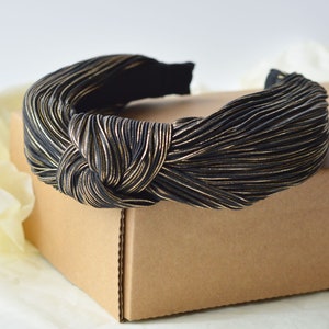 Könnte beinhalten: Ein geknotetes Stirnband in Schwarz und Gold aus Stoff mit plissierter Textur.