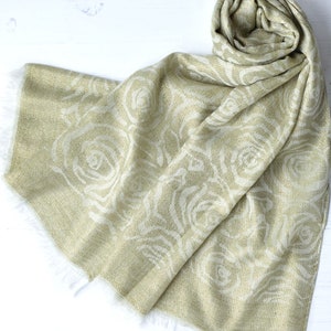 May include: A soft, light green scarf with a white rose pattern. The scarf is made of a lightweight fabric and has a fringed edge.