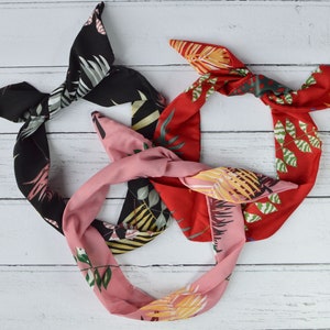 May include: Three fabric headbands with tropical leaf patterns. One headband is black with white and green leaves, one is red with green leaves, and one is pink with green and yellow leaves.
