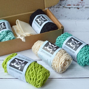 May include: Four reusable produce bags in a box. The bags are made of natural cotton and have a short handle. The bags are in the colors green, beige, teal, and black. The bags have a label that says "Turtle Bags" and "Short Handle".