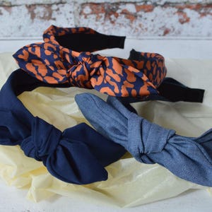 Op de afbeelding: Drie stoffen hoofdbanden met geknoopte strikken. Een hoofdband is donkerblauw, een is denimblauw en een is oranje en zwart met een luipaardprint.