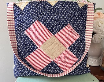 Könnte beinhalten: Eine gesteppte Tragetasche mit Patchwork-Design. Die Tasche hat einen marineblauen Blumendruck, rot-weiß gestreifte Akzente und ein zentrales Rautenmuster in Rot und Beige. Die Tasche steht auf einem hellgrünen Stuhl.