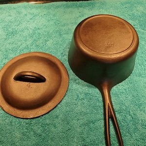 May include: A black cast iron pot with a handle and a lid. The lid is off to the side. The pot has the number "4" on the lid and the letters "ZOT" on the bottom. The pot is sitting on a teal towel.